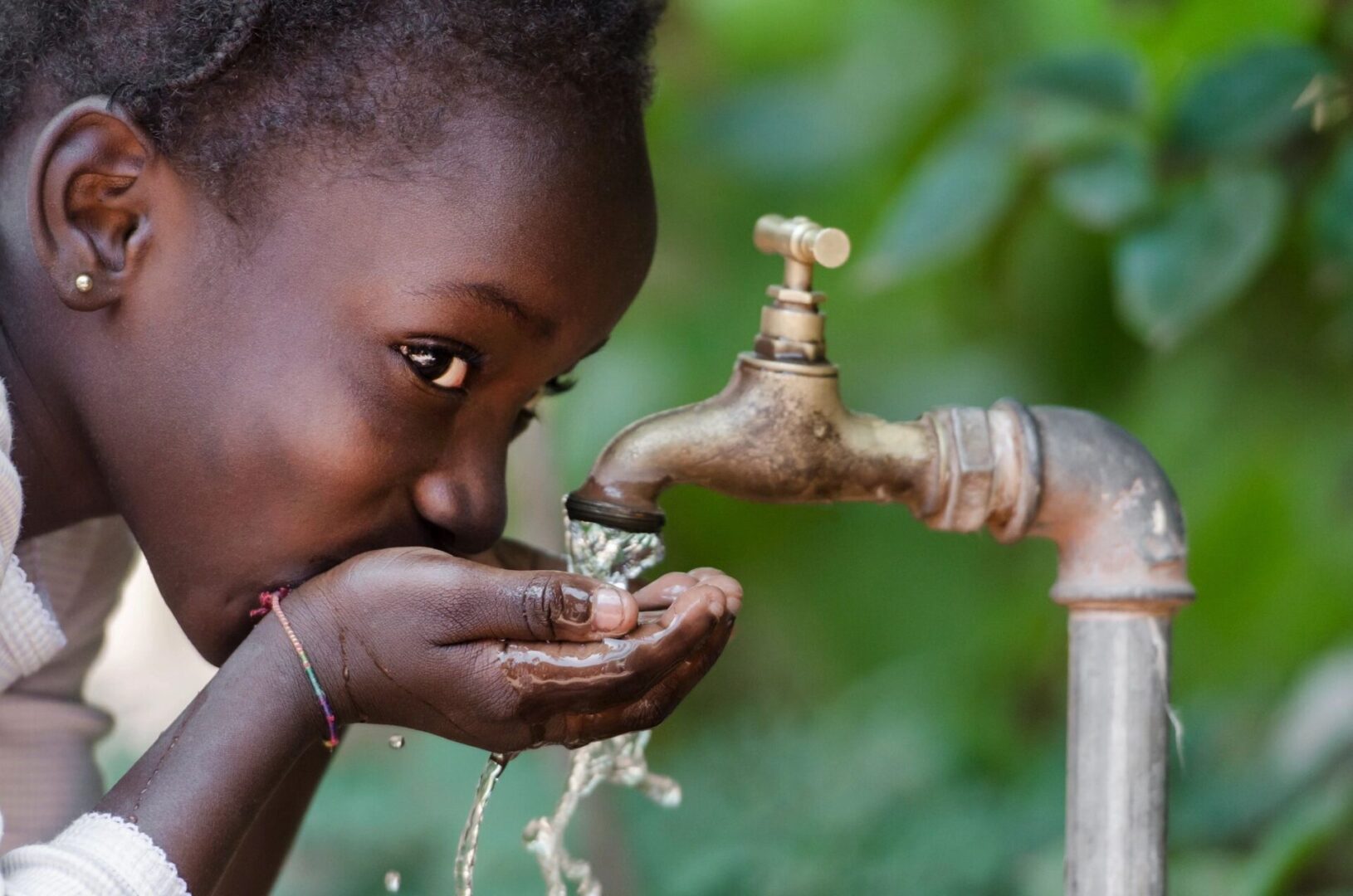 A young girl drinking water from a faucet.